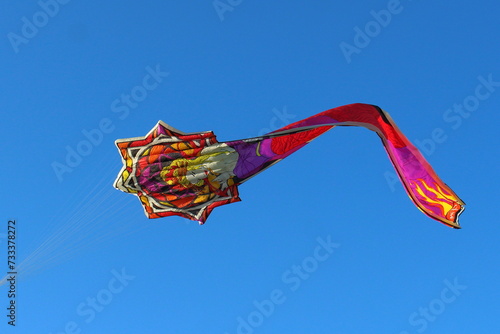 Aquilone raffigurante una donna bionda con i capelli raccolti, disegnata in stile liberty che vola nel cielo blu. La coda dell’aquilone rappresenta un lungo vestito elegante photo