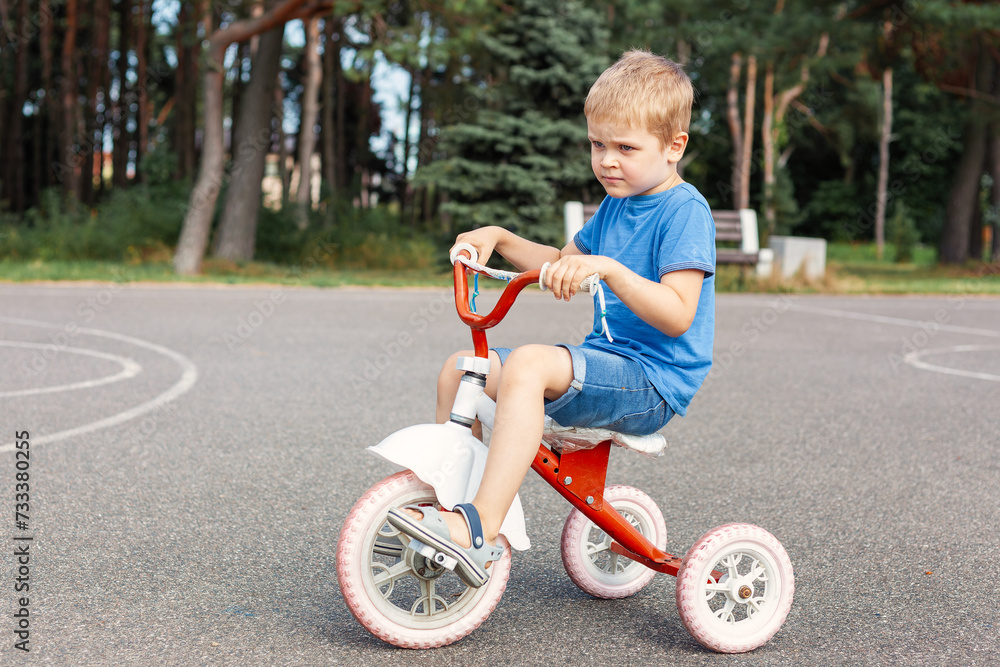 A little boy without a helmet is learning to ride a tricycle in a city park A little boy without a helmet is learning to ride a tricycle in a city park