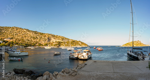 Panorama shot of motor boats parked at a dock named Agios Nikolaos harbour against blue sea and mountain in one of the ionian island of Zakynthos, Greece photo