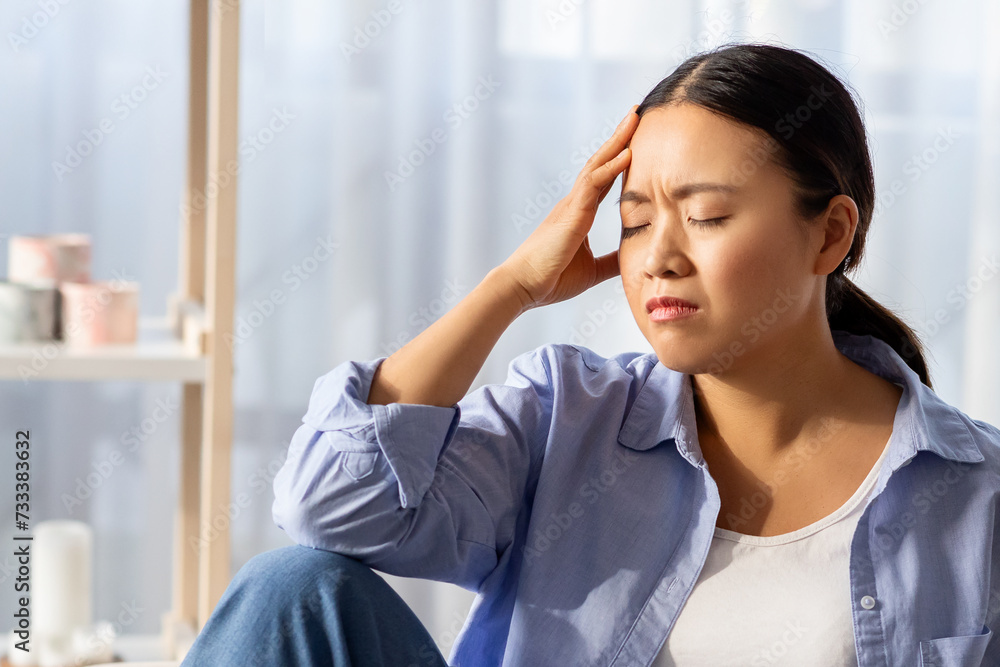 Asian woman with closed eyes touching her head Asian woman with closed eyes touching her head
