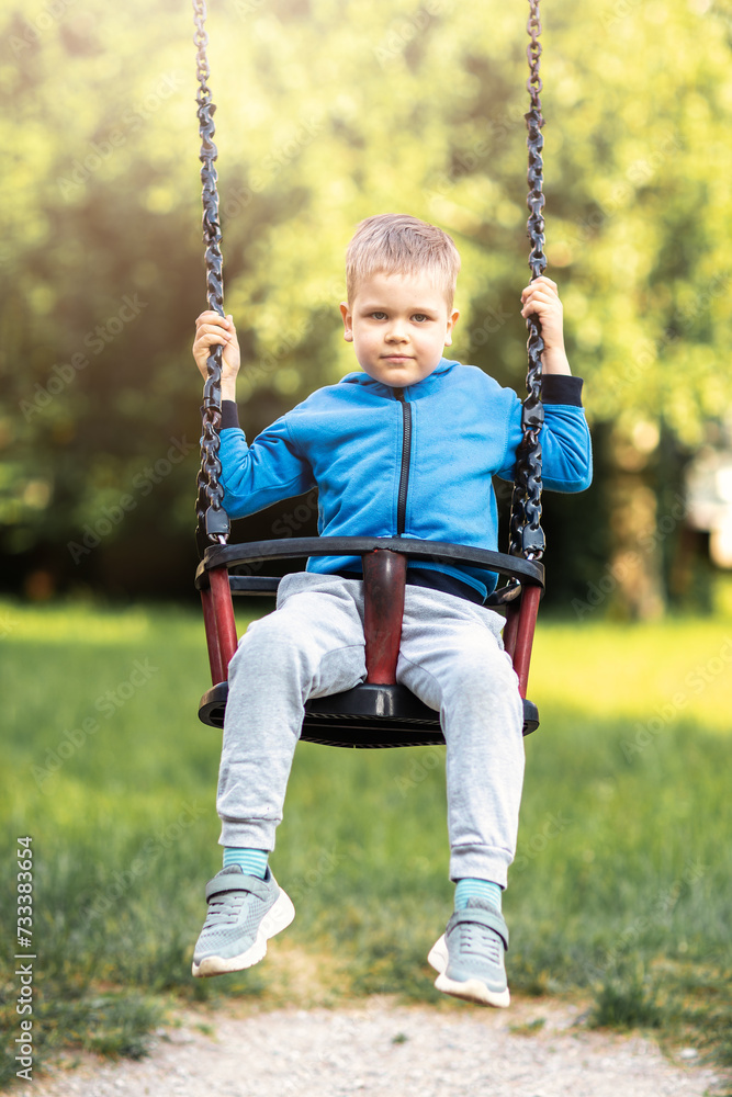 A little boy swings on a hanging swing. Active leisure time with children.