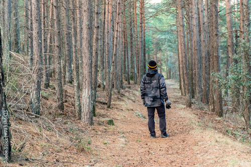 Rear view of a man walking through the forest, wearing a camouflage raincoat and wool hat.