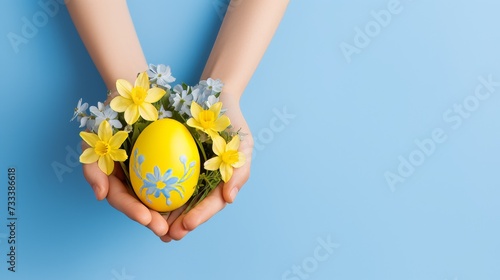 girl s hands holding a hand-painted Easter egg with small spring flowers on a light blue background  Easter holiday concept