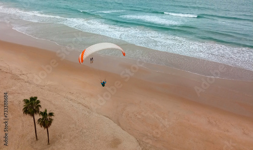 Gleitschimflug landung am Strand mit Menschen und Palmen. photo