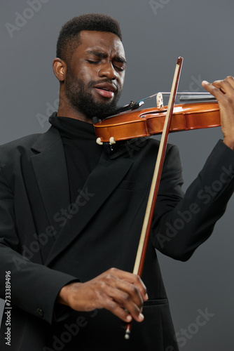 Elegant African American man in black suit playing violin on gray background in studio setting