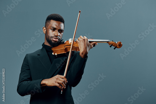 Talented African American man in a suit playing the violin against a neutral gray background