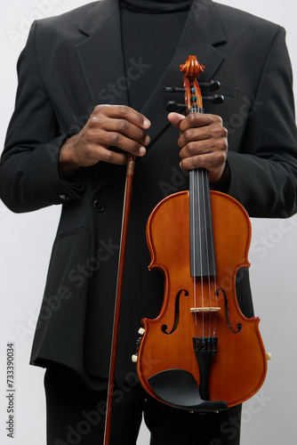 African American man holding violin in black suit standing in front of white background in studio portrait concept