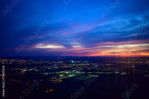 Vista da janela de avião comercial do Rio Iguaçu e Rio Paraná durante voo noturno com luzes da cidade e céu dramático em tons vermelho, roxo e azul. Foz do Iguaçu, Paraná. 2024.
