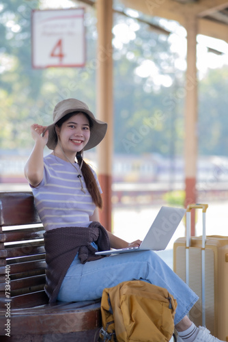 Young Asian woman girl works with a laptop notebook in the train station, Young woman with travel bag sitting on couch using laptop for work, Young freelance working at the train station before travel