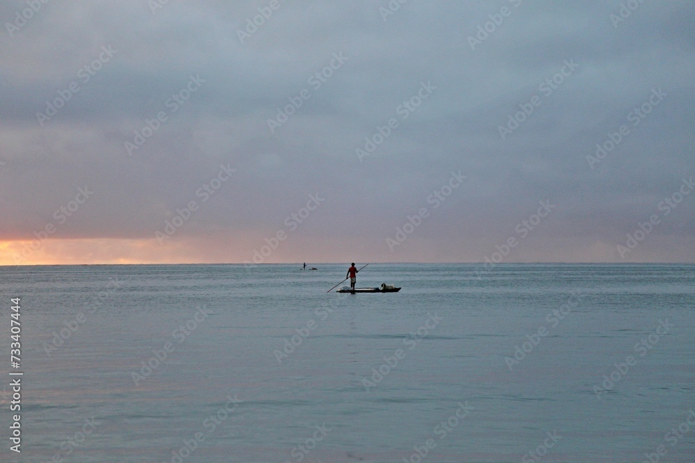 Fototapeta premium A fisherman over a raft in the wide sea water. Early morning day, first sun light. All blue water and sky