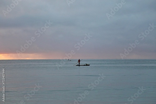 A fisherman over a raft in the wide sea water. Early morning day, first sun light. All blue water and sky