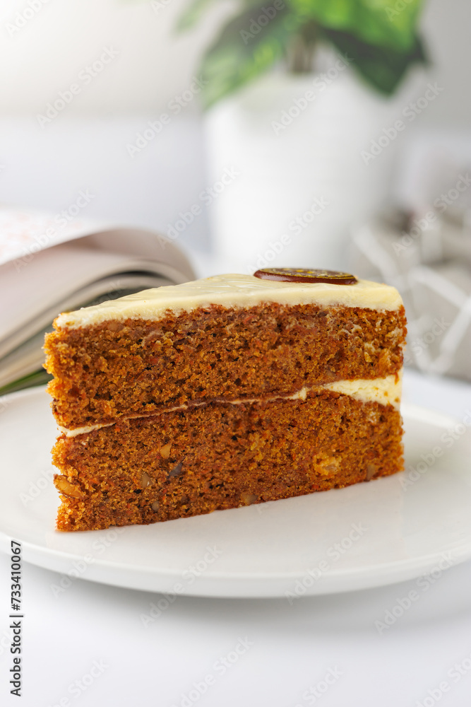 Slice of carrot cake on a white plate with a book in the background Slice of carrot cake on a white plate with a book in the background