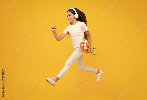 Teen girl 12, 13, 14 years old with skateboard over studio background. Jump and run. Cool modern teenager in stylish clothes. Teenagers lifestyle, casual youth culture. Excited teenager emotions. photo