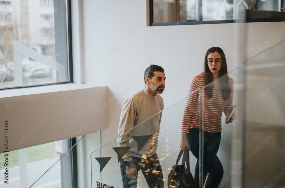 Fototapeta premium Two people in casual wear walking upstairs in a modern office building.