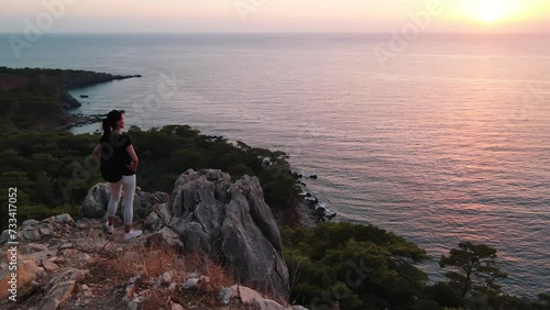 Wallpaper Mural Young woman walking on high sheer cliff on seacoast at sunset. Female hiker climbing a mountain observing seascape Torontodigital.ca