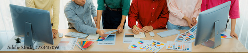 A top view cropped imaged of creative graphic team selects colors carefully from color wheel and palette on table at modern studio, surrounded by graphic documents and materials. Variegated.