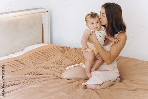 Happy mother with her beautiful little baby daughter in the bedroom on the bed