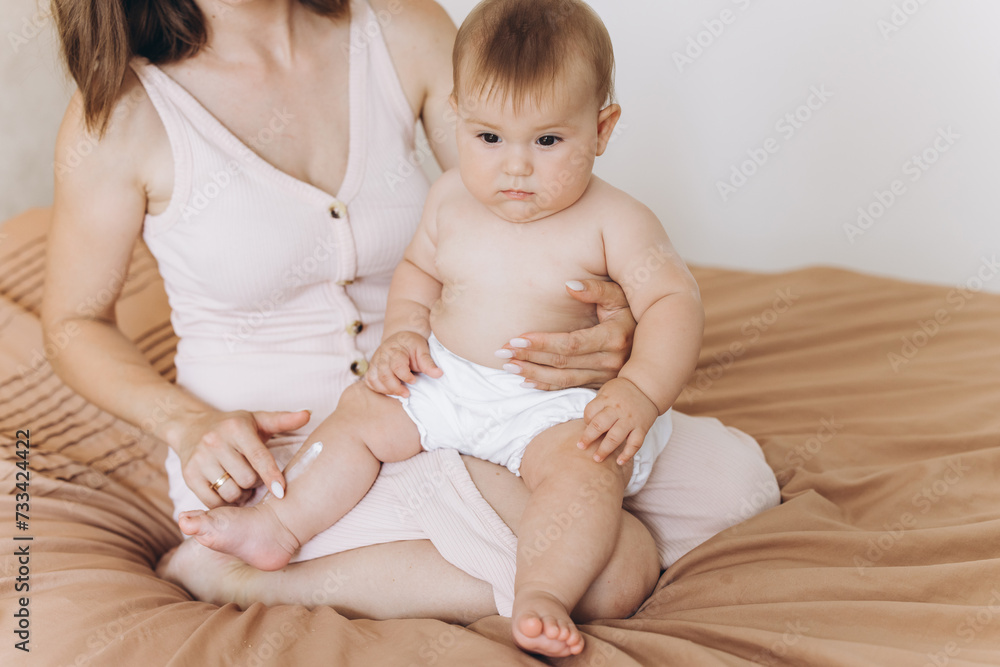 Happy mother applying cream on her baby girl's body Happy mother applying cream on her baby girl's body