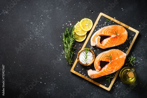 Fresh fish. Salmon steaks on cutting board at black background. Top view with ingredients for cooking. photo