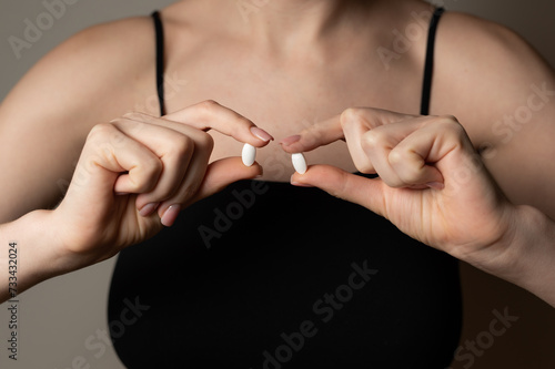 Woman hands hold two pills tabs medicine to kill pain, self help supplements concept, prescribed medicine