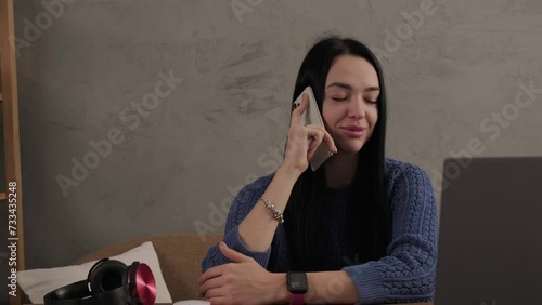 The girl is talking on the phone while sitting at the laptop in the room