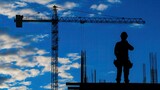 Sylwetka robotnika stoi na placu budowy przed dźwigiem na tle chmur.