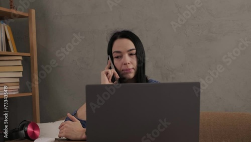 The girl is talking on the phone while sitting at the laptop in the room