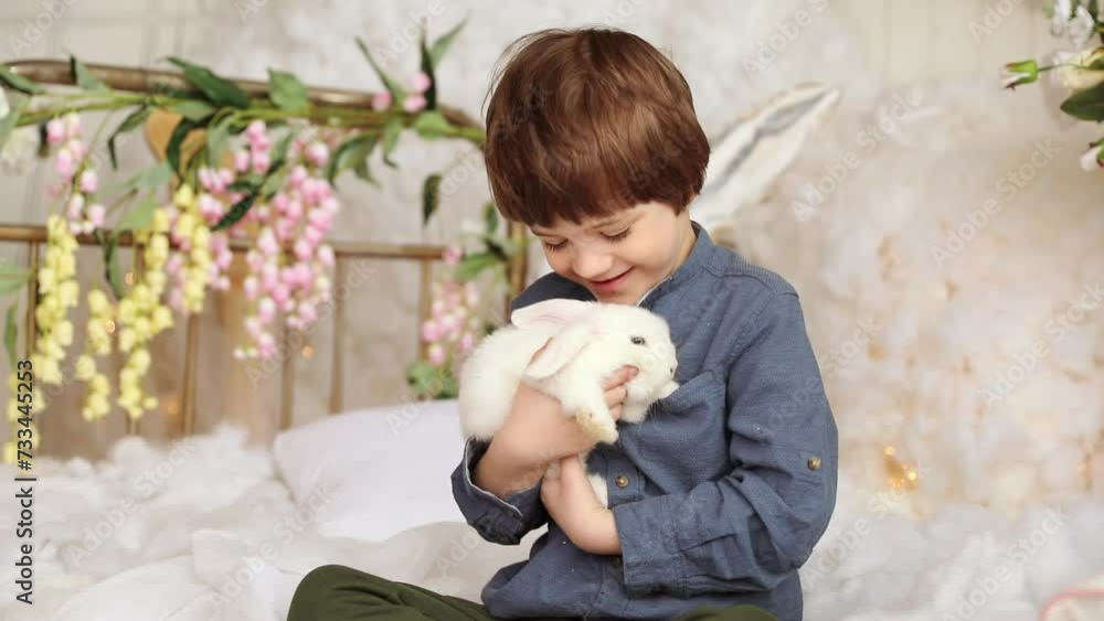 White Easter rabbit sits on the hands of a little boy, who huggs the rabbit White Easter rabbit sits on the hands of a little boy, who huggs the rabbit