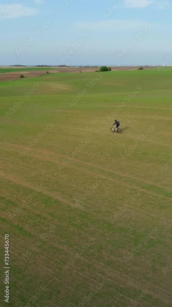 Vertical video. Aerial view. Riding an MTB bike on a spring field. A sports trip by an adult man through the landscapes of nature. Vertical video. Aerial view. Riding an MTB bike on a spring field. A sports trip by an adult man through the landscapes of nature.