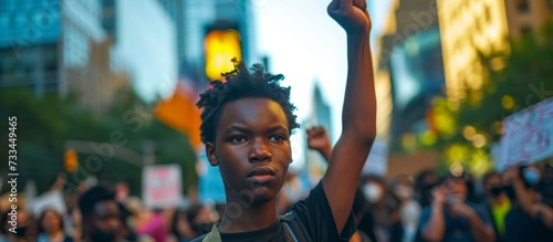 A young person with dark skin raises a defiant fist at a city protest.