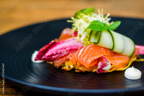 Salmon appetizer starter on a black plate on a wooden table in a restaurant