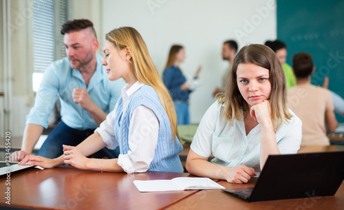 Upset girl sitting at table in auditorium during break on background with other students