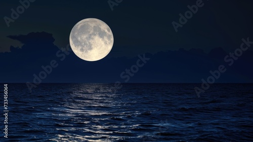 A full moon rising over a body of water. © tilialucida