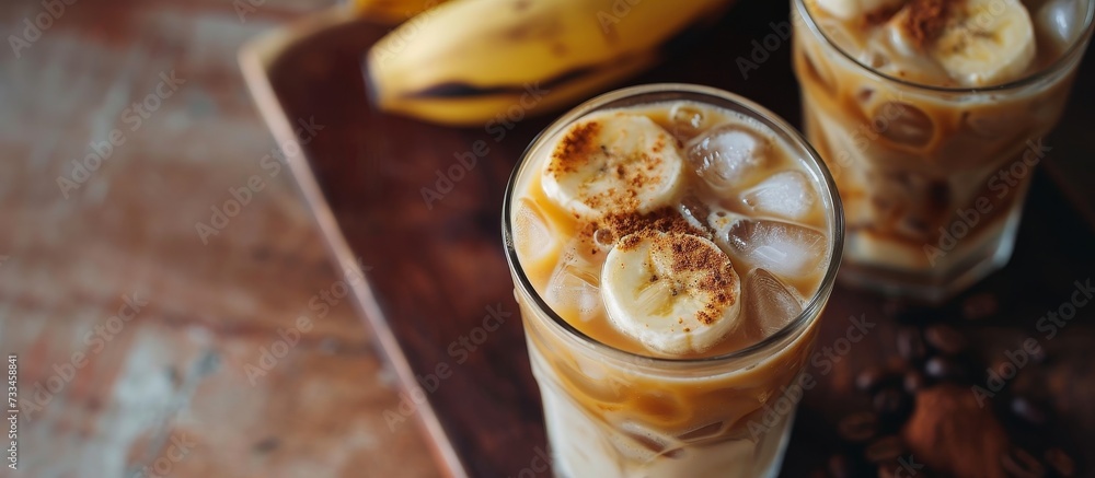 Two glasses of iced coffee garnished with banana slices, placed on a rustic wooden table. A comforting drink perfect for a relaxing moment. Two glasses of iced coffee garnished with banana slices, placed on a rustic wooden table. A comforting drink perfect for a relaxing moment.