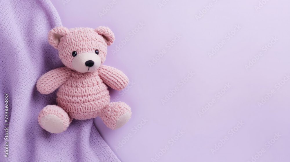 Fototapeta premium A small knitted amigurumi bear toy on a purple blanket, on a purple background. Flat lay, top view, copy space. space for text