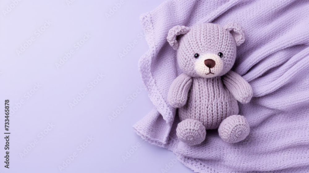 Fototapeta premium A small knitted amigurumi bear toy on a violet blanket, on a violet background. Flat lay, top view, copy space. space for text