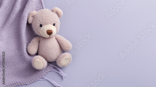 A small knitted amigurumi bear toy on a purple blanket, on a purple background. Flat lay, top view, copy space. space for text