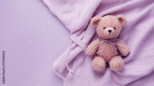 A small knitted amigurumi bear toy on a purple blanket, on a purple background. Flat lay, top view, copy space. space for text © Irina B