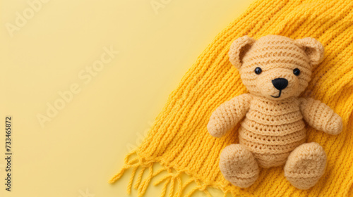 A small knitted amigurumi bear toy on a yellow blanket, on a yellow background. Flat lay, top view, copy space. space for text photo