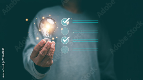 Concept of successful business and thinking solution strategy. Businessman holding glowing light bulb and have checklist for solving problem. Check and solution list to business target.