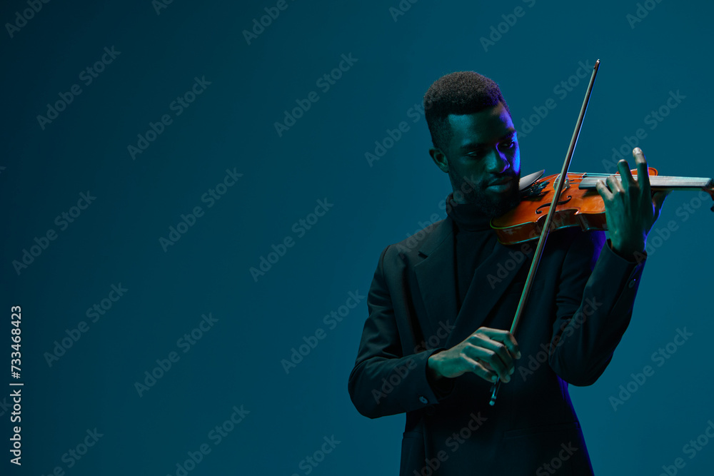 Fototapeta premium Elegant musician in black suit playing melodious violin against vibrant blue background, artistic performance concept