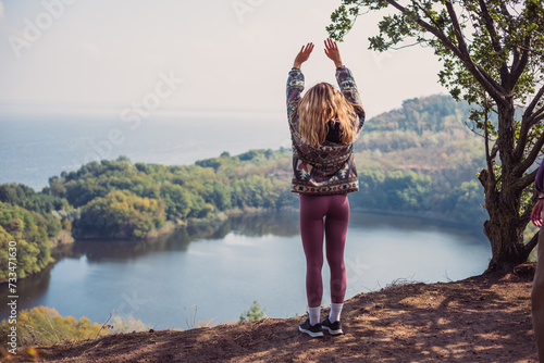 Beautiful young woman standing in front of wonderful lake with her hands up, enjoying the mindful moment