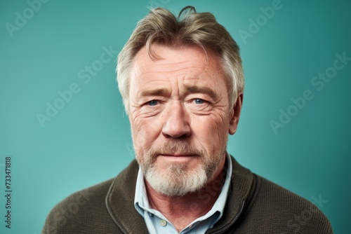 Portrait of a senior man with grey hair and beard on a blue background.