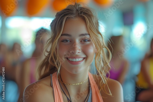 A stunning woman with a bright smile and long, layered hair looks effortlessly stylish as she gazes confidently at the camera, her necklace accentuating her throat and her fashion accessory adding a 