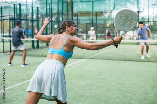 Attractive woman padel tennis player training on court. Rear view of young woman using racket to hit ball. © JackF