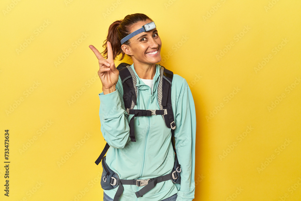 Mountain gear and frontal light on yellow joyful and carefree showing a peace symbol with fingers. Mountain gear and frontal light on yellow joyful and carefree showing a peace symbol with fingers.
