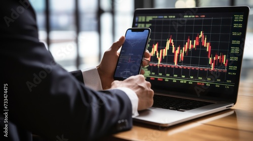 Hands of a person engaged in online trading on a smartphone with laptop background