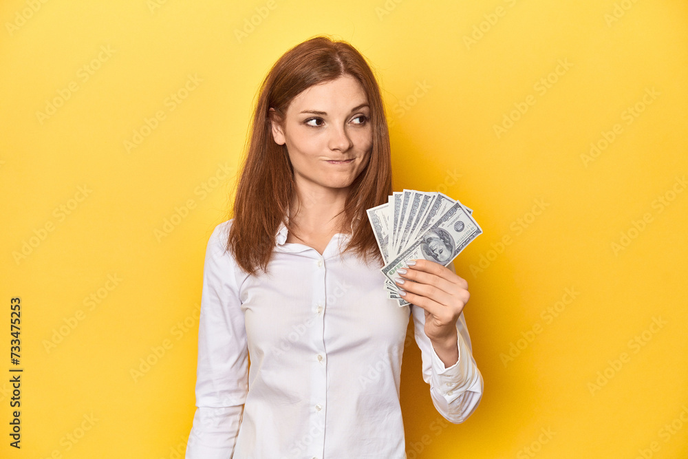 Redhead with dollar bills, cash in hand confused, feels doubtful and unsure. Redhead with dollar bills, cash in hand confused, feels doubtful and unsure.