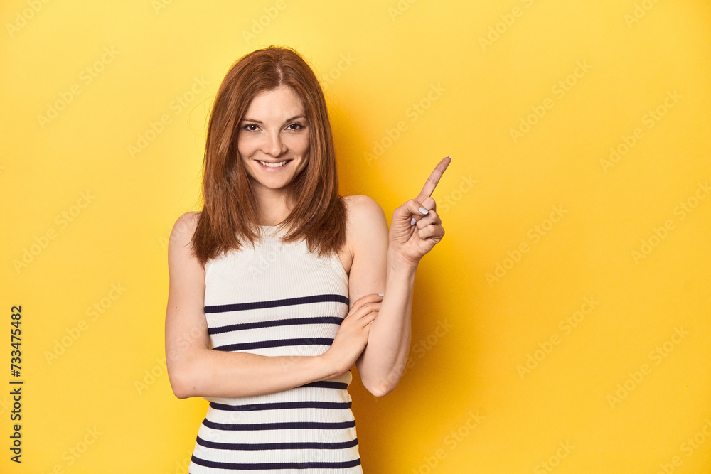 Redhead in a tank top, casual studio shot smiling cheerfully pointing with forefinger away. Redhead in a tank top, casual studio shot smiling cheerfully pointing with forefinger away.