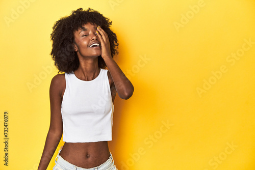 Teen girl in white tank top, yellow studio background laughing happy, carefree, natural emotion.